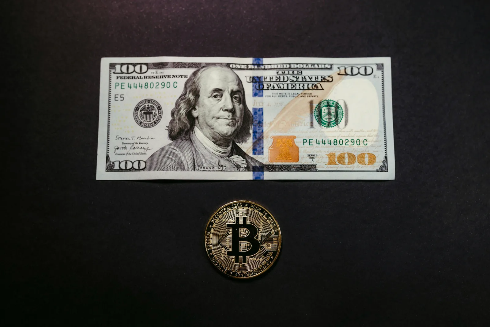 US one-hundred-dollar note and a physical Bitcoin token.