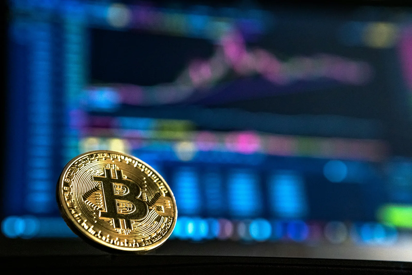 Physical Bitcoin coin in front of cryptocurrency trading monitors.
