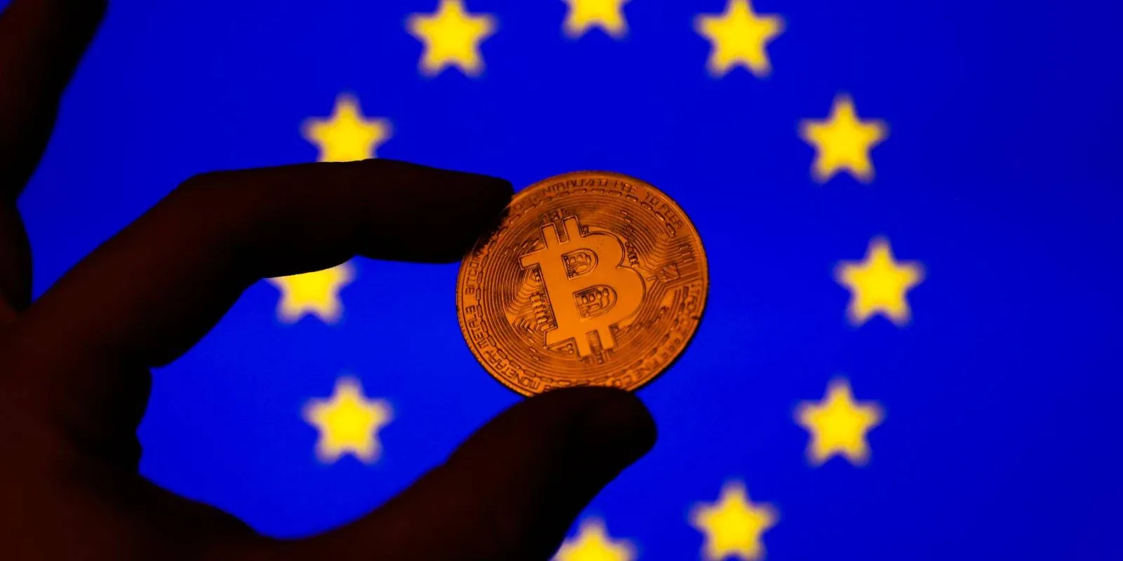 Hand holding a Bitcoin coin against the European Union flag.